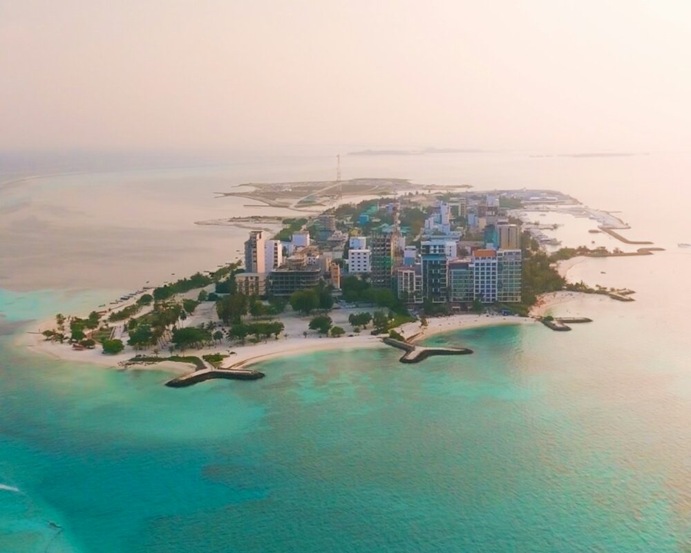 Aerial view of a developed Maldivian local island, its multistorey buildings ringed by a turquoise lagoon